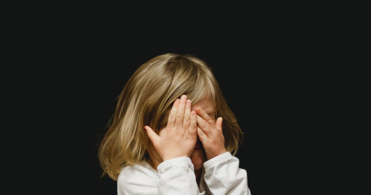 toddler crying and hiding behind hands