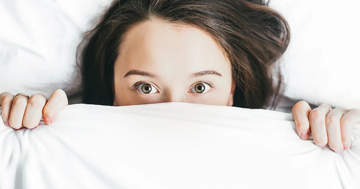 woman hiding under blanket with eyes focused on camera
