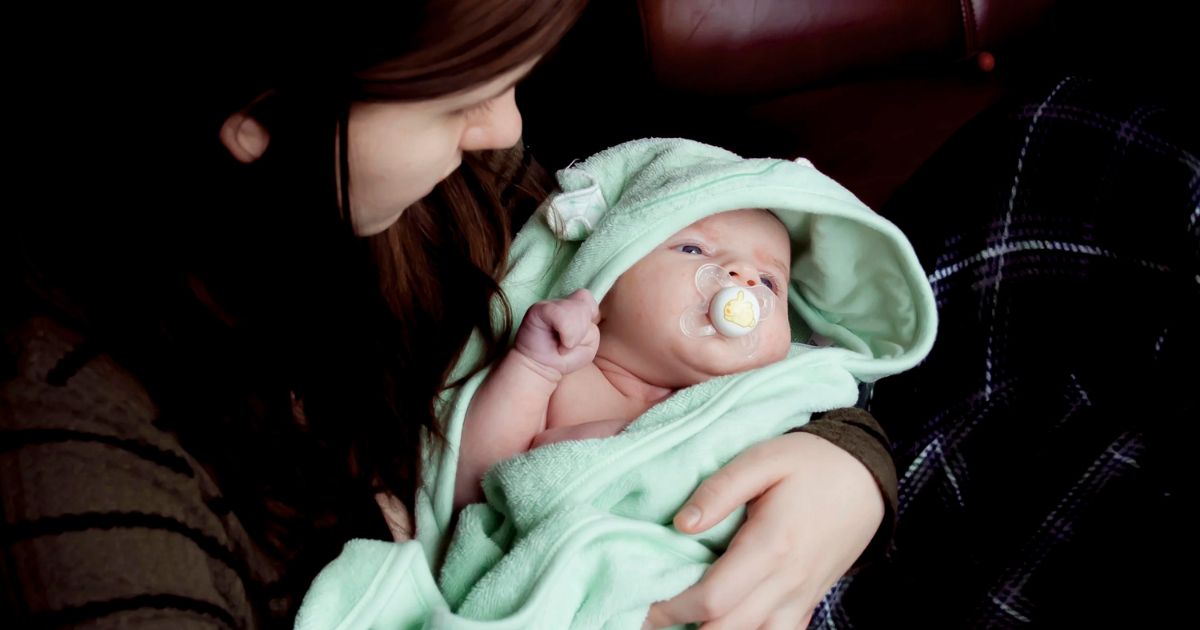 mom holding baby wrapped in green blanket with pacifier