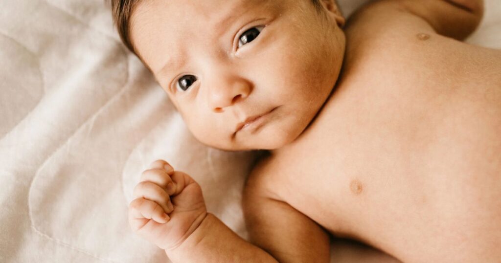 awake baby laying on sheet