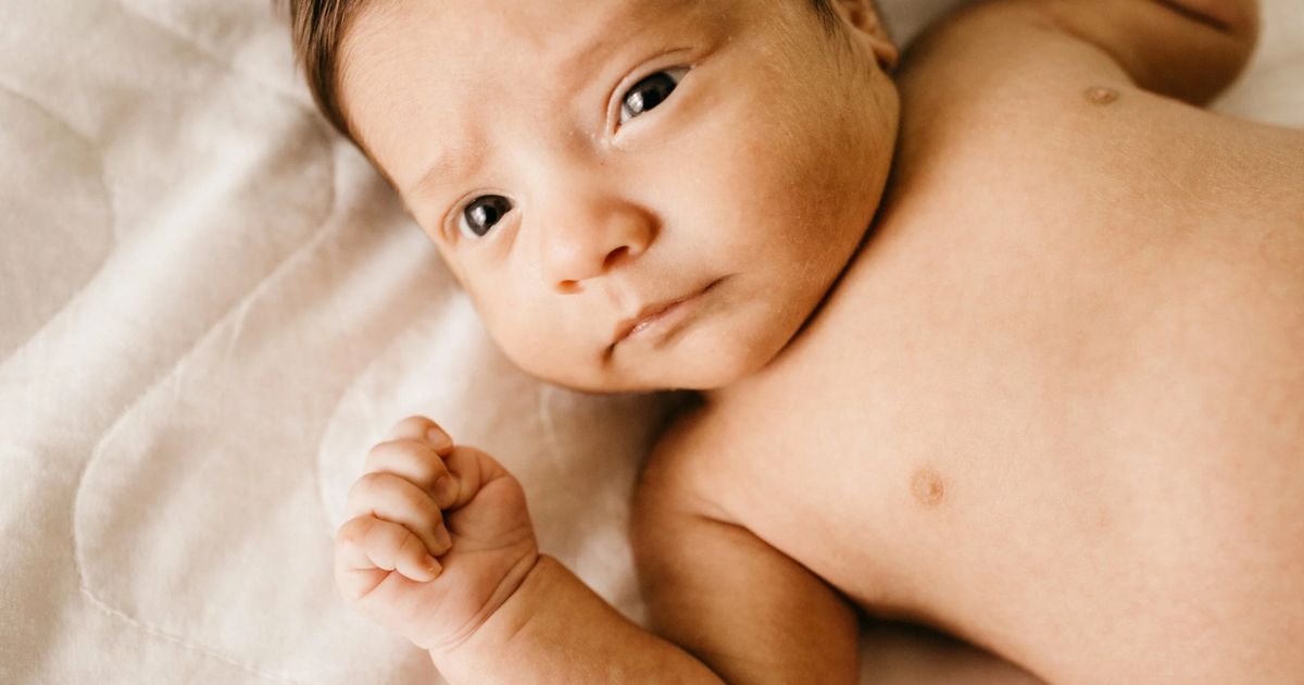 awake baby laying on sheet